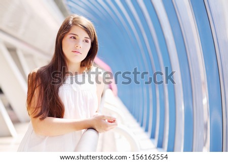 Dreaming girl in white blouse stands in long blue gallery and looks in windows.