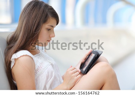 Pretty girl in white blouse looks at tablet pc on floor in light long gallery.