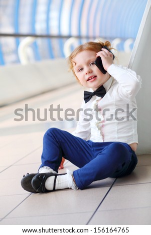 Red hair little cute girl talks by cell phone on grey floor.