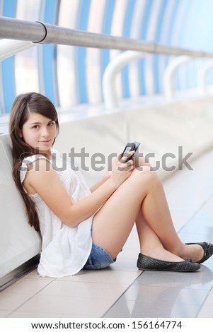 Pretty girl in white blouse with tablet pc sits on floor and looks at camera in light gallery.