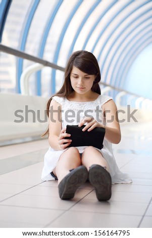 Pretty girl in white blouse holds tablet pc in light long gallery.