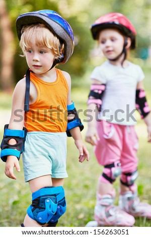 Two kids in rollers and protective equipment stand half-turned and looking back, focus  on boy