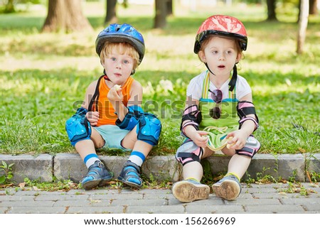 Tired little scooterists rest sitting on curb of walkway in park
