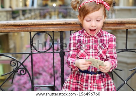 Little cute girl with papers stands near wrought railings and admires.