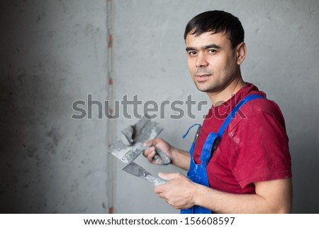 A man with spatula in workwear makes repairs the wall