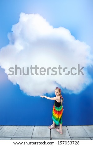 Little smiling girl holds large painted at blue wall cloud and looks up.