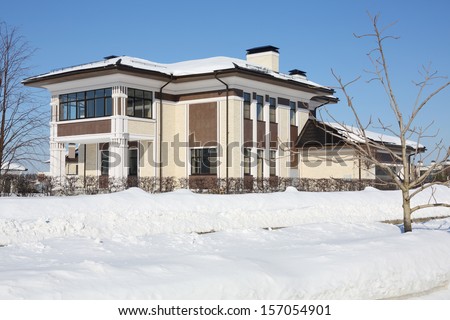 Brown and yellow cottage with garage and loggia at frosty and sunny winter day.