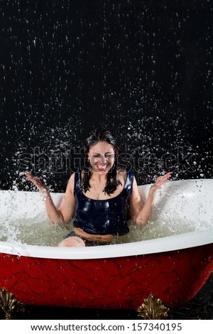 Smiling girl with closed eyes splashes water in the bathtub under the spray