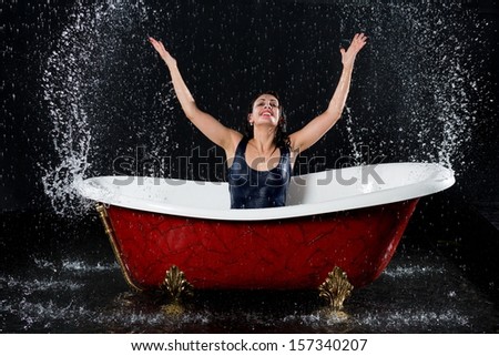 Drenched girl splashes water in the bathtub under the spray