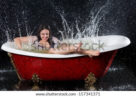 Wet girl with closed eyes have funr in the bathtub under the spray