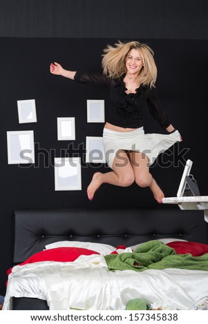 Cheerful girl in a white skirt jumping on the bed in the room with empty frames on the wall