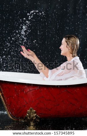 Wet girl in a blouse have fun in the bathtub under the spray of water