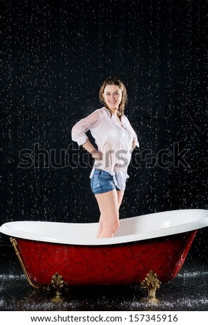 Drenched girl in a blouse stands in the bathtub under the spray of water