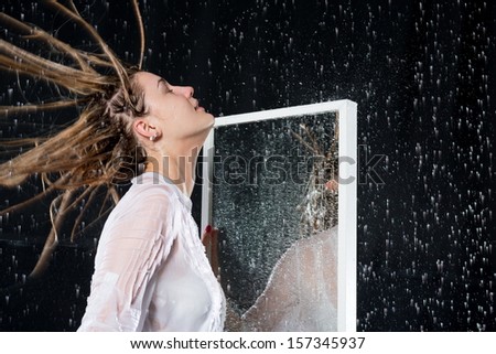 Wet girl with disheveled hair under the spray of water near the mirror