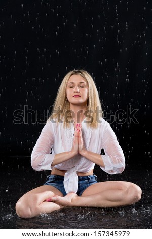 Wet girl in lotus pose meditating under the spray of water