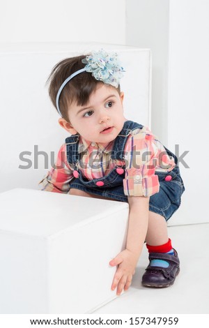 Little girl with a hair band on the head is playing with the white cube in a studio
