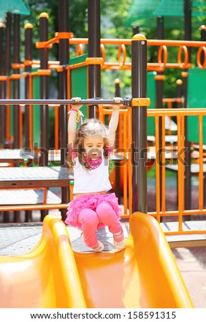 Little girl holds on to the railing to roll down hill on the playground