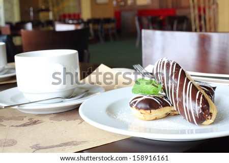 Eclairs with cream in chocolate coating on a plate and tea in cafe