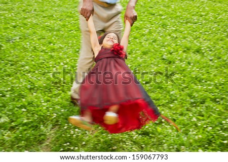 Father turns little daughter in circle holding her hands on sunny grassy lawn in park