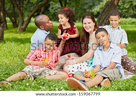 Happy Family Of Six Sits On Rag Matting And Eats Fruits And Berries In Summer Park