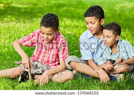 Portrait of three boys-brothers who sit together on grass in park on summer day
