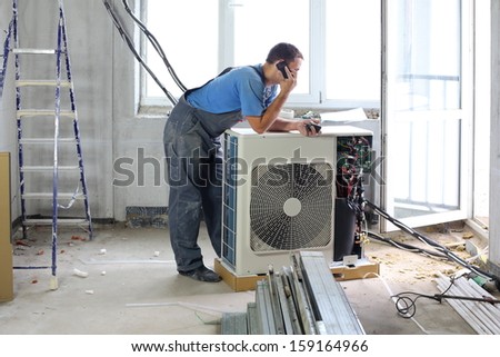 A worker sets air conditioner in apartment and talking on the phone