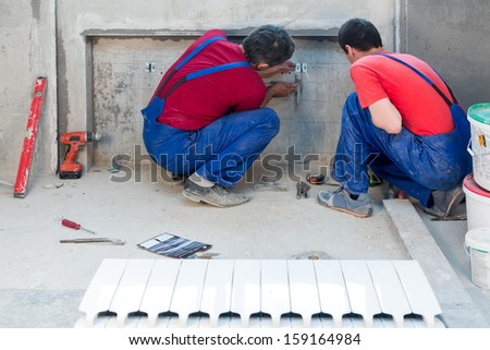 Two workers have made fastening in a niche for radiators in apartment with a rough finish