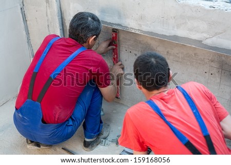 Two workers have made a niche for radiators in apartment with a rough finish