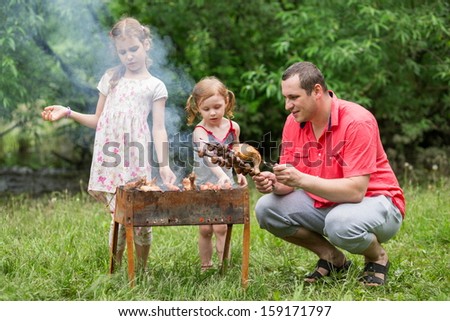 A family of three making barbecue on the grill on nature, focus on a father.