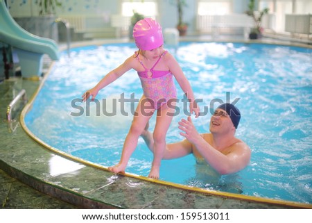 Little girl jumping into the pool, her father in the pool catches her
