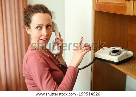 Young woman talking on a rotary phone and ask keep quiet finger gesture