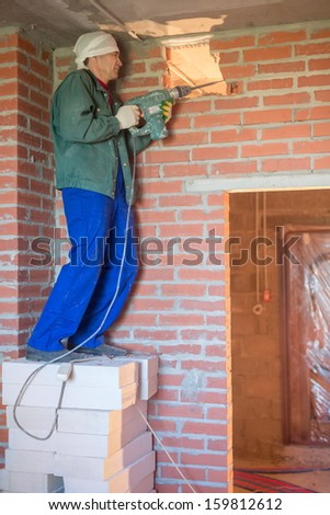 The worker in workwear makes a hole in the wall with a large perforator