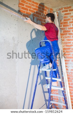 A worker on the ladder in workwear makes repairs the wall