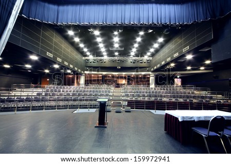 Stage with desk and rows of chairs  in modern black hall for business meetings.