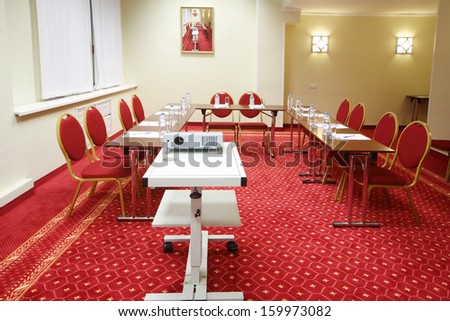 Projector, red chairs and tables in small room with red carpet for business meetings.