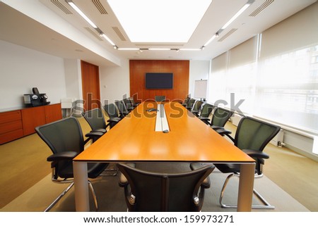 Long wooden table, modern armchairs and tv in light room for business meetings.