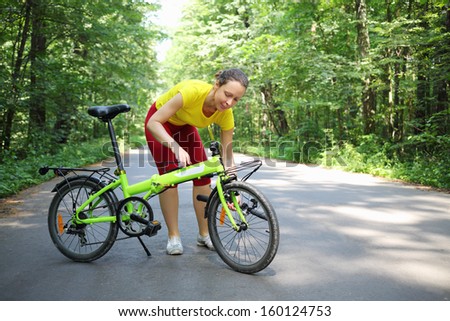 Young woman in sport clothes converts bicycle handle bar in park at sunny day.