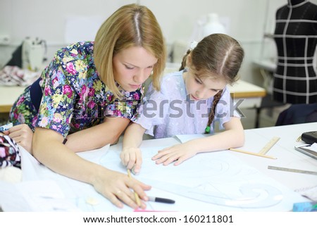 Female tailor teaches student girl how to draw patterns for clothes. Focus on girl.