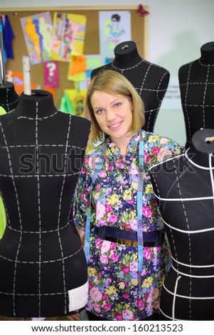 Happy female tailor stands among five black mannequins in her studio.