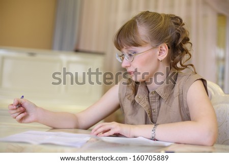 Beautiful girl in glasses sits at table with documents and thinks.