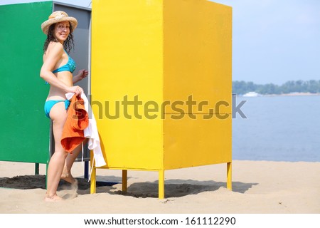 Young beautiful woman in a hat comes in the changing cabin on the beach