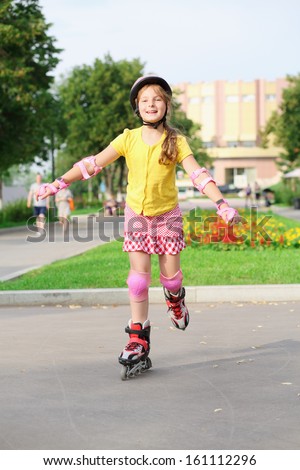 Girl in a helmet, elbow pads and knee pads roller-skating in the park
