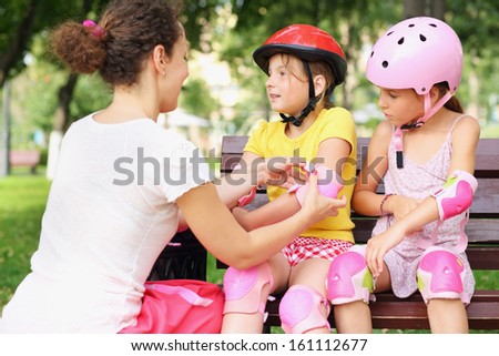 Young woman helping to put on elbow pads two girls in a park