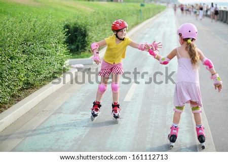 Two girls in roller skates, knee and elbow pads ride on rollers and give each other a high five