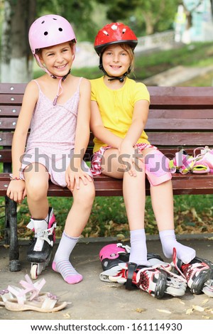 Two girls sitting on the bench and put on rollers and protective knee and elbow pads