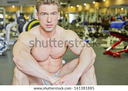 Bodybuilder sits on floor in gym hall taking rest