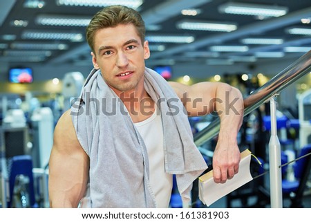 Portrait of smiling bodybuilder who stands with towel on his shoulders and scratchpad in hand