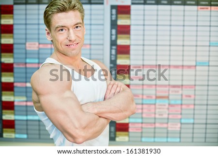 Half-length portrait of bodybuilder who stands half-turned with his arms crossed on chest against training schedule