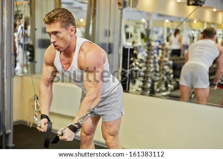 Bodybuilder does shoulders exercises against mirror on  wall in gym hall