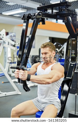 Man bodybuilder does shoulders exercises in gym hall